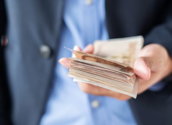 businessman-hand-holding-thai-baht-banknote-stack-min-scaled