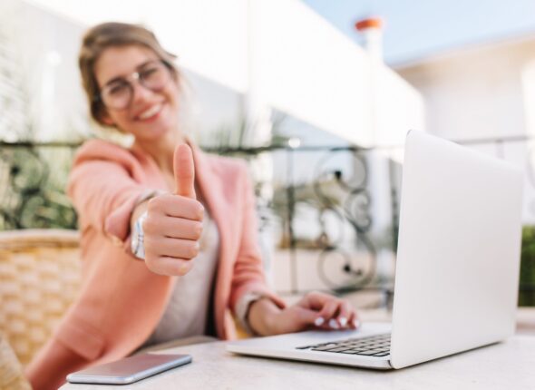 cute-young-woman-student-business-lady-showing-thumbs-up-well-done-sitting-outdoor-cafe-terrace-with-laptop-wearing-pink-smart-clothes-min-scaled